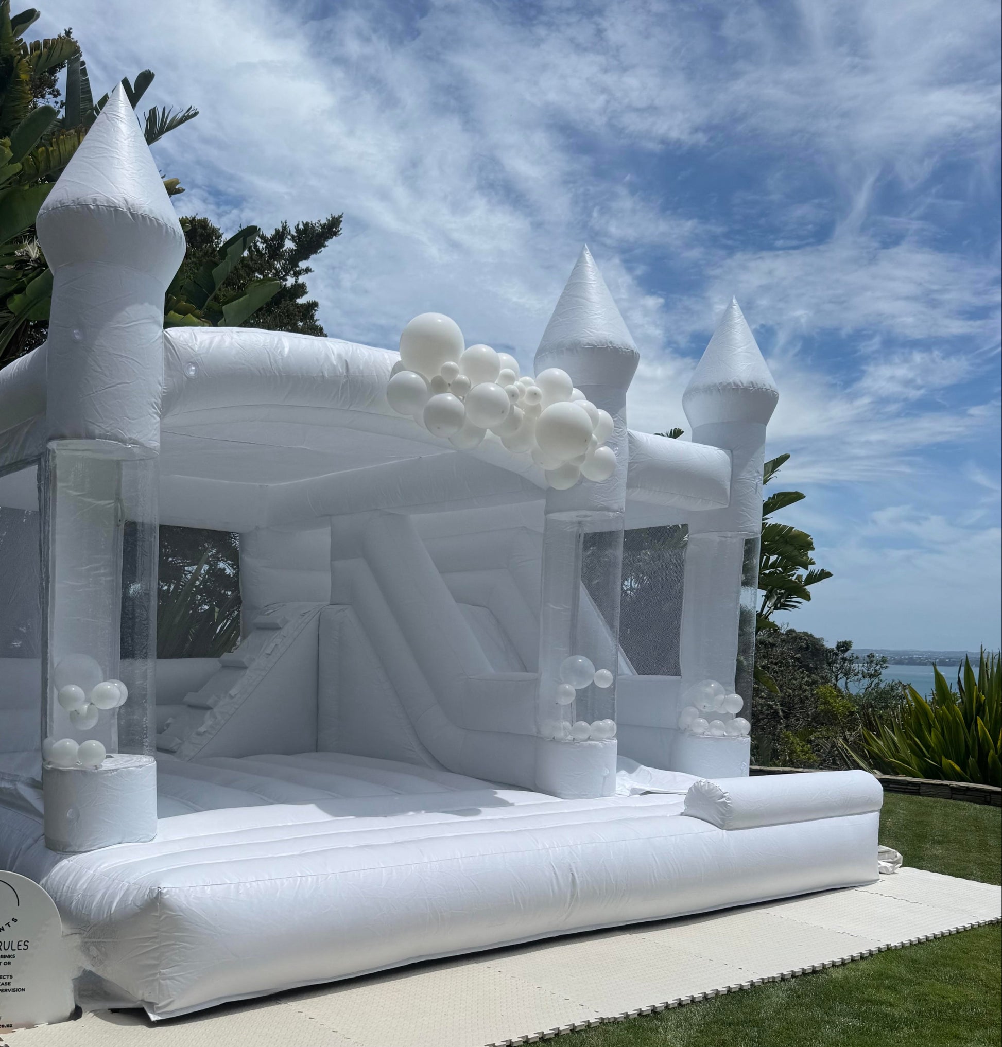 White inflatable castle on grass with trees and blue sky in the background